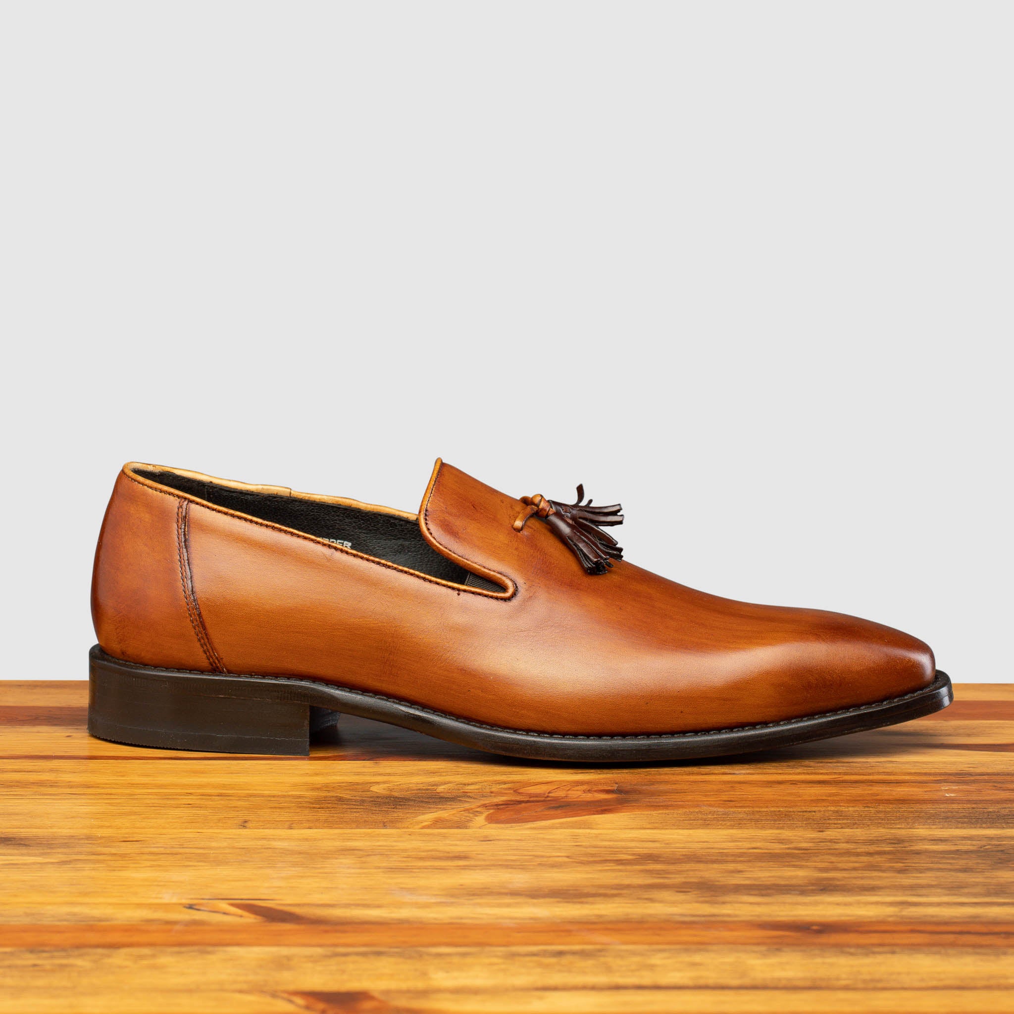 Side profile of Z993 Calzoleria Toscana Dark Caramel David Tassel Slip-On on top of a wooden table